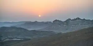 תמונת שקיעה מרהיבה במדבר מכתש רמון עם שמש כתומה מעל ההאדמה הלבנה של המכתש